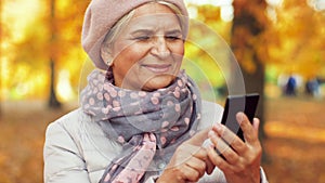 Happy senior woman with smartphone at autumn park