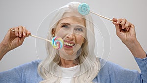 Happy senior woman smiling in studio. Old lady playing with candy indoors.