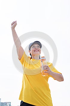 Happy senior woman in sports clothes exercising in the park standing with arms up