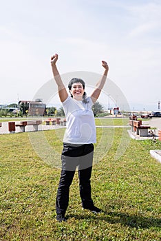 Happy senior woman in sports clothes exercising in the park standing with arms up