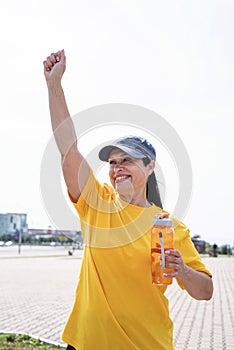 Happy senior woman in sports clothes exercising in the park standing with arms up