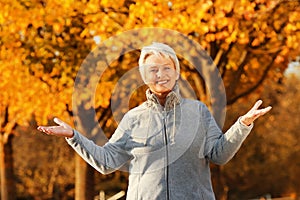 Happy senior woman with spread arms in front of autumn trees