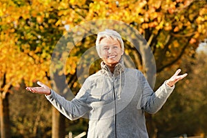 Happy senior woman with spread arms in front of autumn trees