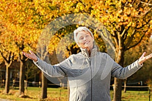 Happy senior woman with spread arms in front of autumn trees