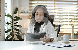 Happy senior woman surfing internet, checking email on digital tablet