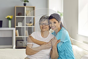 Happy senior woman together with her home care nurse or caregiver smiling at camera