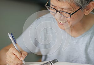 Happy senior woman wearing glasses handwriting memo of the day, letters, or diary smiling.