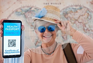 Happy senior woman wearing straw hat shows health passport app for people vaccinated against coronavirus, ready to travel