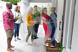 Happy senior woman welcoming multiracial friends at entrance during house party