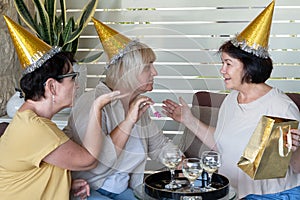 Happy senior women wearing party hats drinking wine together and send air kiss at restaurant.