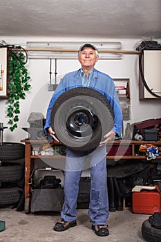 Happy senior worker changing tire in garage