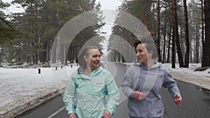 Happy Senior and young Caucasian women running in the snowy park in winter talking and smiling. Close up Front follow shot. Slow M