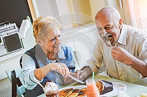 Happy seniors couple eating pancakes in a bar restaurant - Mature people having fun dining together at home