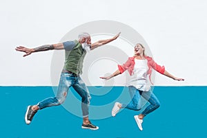 Happy seniors crazy couple jumping together outdoor - Mature trendy people having fun celebrating and dancing outside