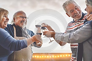 Happy seniors friends drinking red wine on terrace sunset - Mature people having fun laughing and sharing time together outdoor