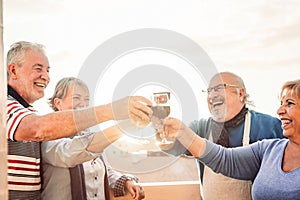 Happy seniors friends drinking red wine on terrace sunset - Pensioners people having fun enjoying time together outdoor