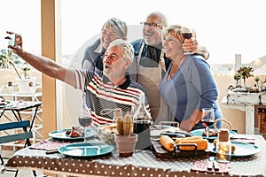 Happy seniors friends taking selfie with mobile smartphone camera at dinner on terrace - Retired people having fun eating