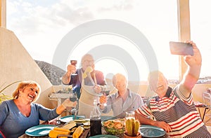 Happy seniors taking a selfie with mobile phone and making a barbecue on the rooftop