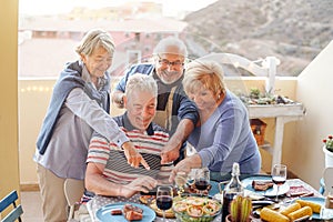 Happy seniors watching on mobile smart phone at dinner on terrace - Retired people having fun dining together