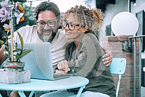 Happy serene couple in love using laptop together at home in the garden smiling and having fun. Man and woman watching computer