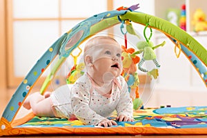 Happy seven months baby girl plays lying on colorful playmat photo