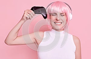 Happy sexy gamer girl with pink hair playing video games using joystick