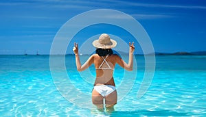 Happy sexy woman in white bikini and straw hat showing peace sign with both hands relax in turquoise sea