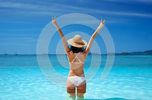 Happy sexy woman in white bikini and straw hat showing peace sign with both hands relax in turquoise sea water on