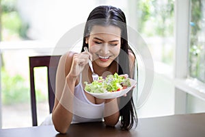 Happy sexy young asian woman in white singlet smiling and eating  fresh organic salad . A beautiful girl have breakfast healthy