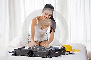 happy sexy young asian woman in white singlet smiling packing her suitcase sitting on the bed at bedroom . A beautiful girl