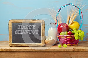 Happy Shavuot greeting design with milk and fruits basket on wooden rustic table.