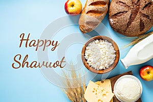 Happy Shavuot Jewish holiday concept. Dairy products, wheats, cottage cheese in bowl, cheese, bread, apples, bottle of milk on