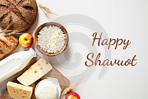 Happy Shavuot Jewish holiday greeting card, poster. Flat lay cottage cheese, bread, milk bottles, cheese, apples, wheat on white