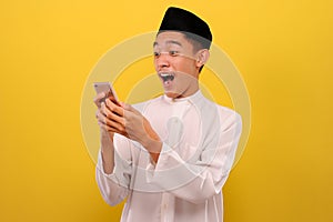 Happy Shock Young Asian Muslim man wearing muslim clothes holding mobile phone look at phone screen