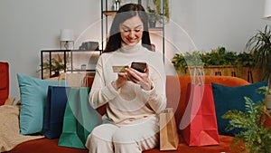 Happy shopaholic young woman girl sitting with shopping bags making online payment with credit card