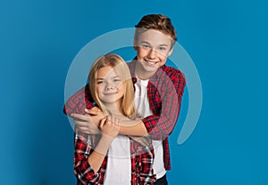 Happy siblings, brother and sister hugging and posing over blue background