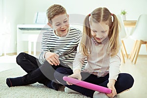 Happy siblings children playing with tablet on floor at home