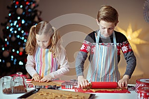 Happy siblings children preparing Christmas cookies at home with christmas tree on background