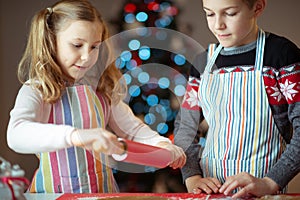 Happy siblings children preparing Christmas cookies at home with christmas tree on background