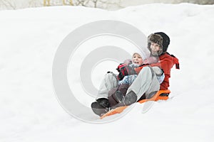 Happy siblings having downhill fun on winter orange plastic snow slider