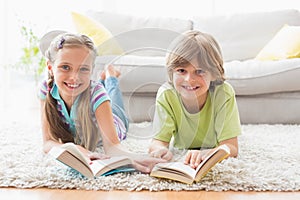 Happy siblings holding books while lying on rug