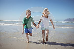 Happy siblings holding hands while running at beach