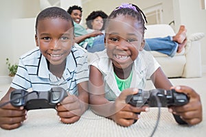 Happy siblings lying on the floor playing video games