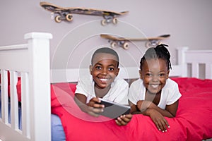 Happy siblings with mobile phone lying on bed at home