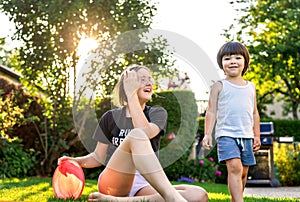 Happy siblings playing frisbee on green grass in garden backyard at sunset. Togetherness, little brother spending time with teen s