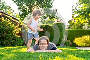 Happy siblings playing on green grass in garden backyard at sunset.