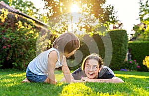 Happy siblings playing on green grass in garden backyard at sunset. Togetherness, little brother spending time with his teen siste