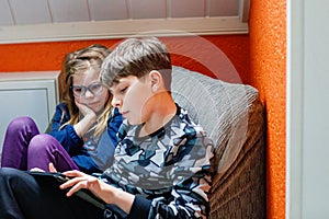 Happy siblings playing on tablet together. Little sister girl and teenager boy playing game at home. Two children.