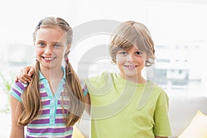 Happy siblings standing arm around at home