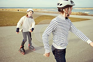 Happy siblings teenager boy and girl having fun during inline skating at sunny day at Baltic sea promenade